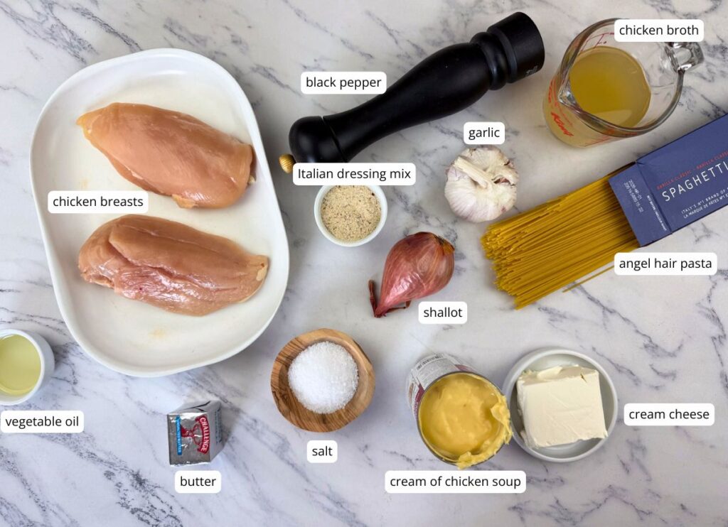 Ingredients for a chicken pasta dish arranged on a marble surface, including raw chicken breasts, pasta, seasonings, dairy, broth, garlic, and shallot, each labeled.