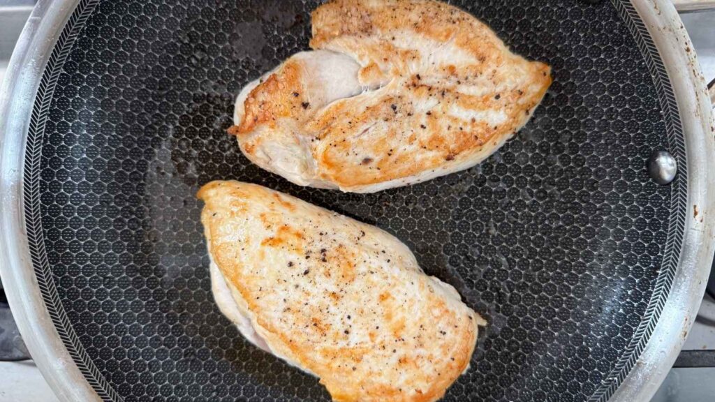 Two seasoned chicken breasts are being cooked in a frying pan.