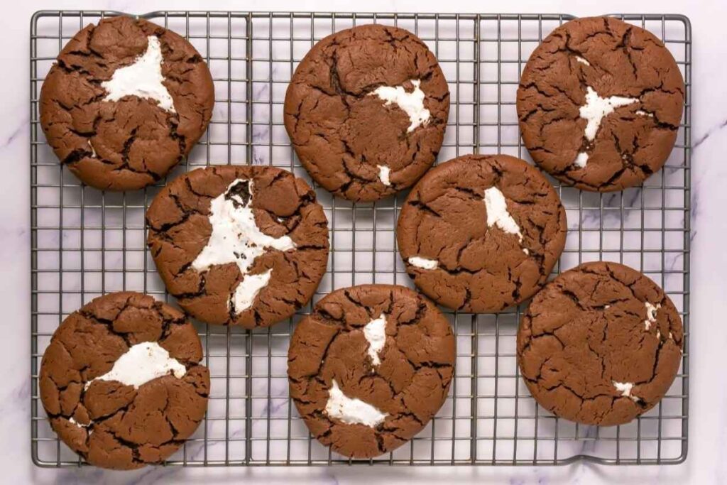 Eight chocolate cookies with white marshmallow centers cooling on a wire rack, viewed from above.