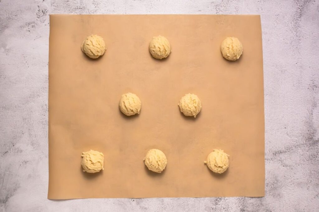 Nine evenly spaced balls of cookie dough are arranged in a grid pattern on a parchment-lined baking sheet.