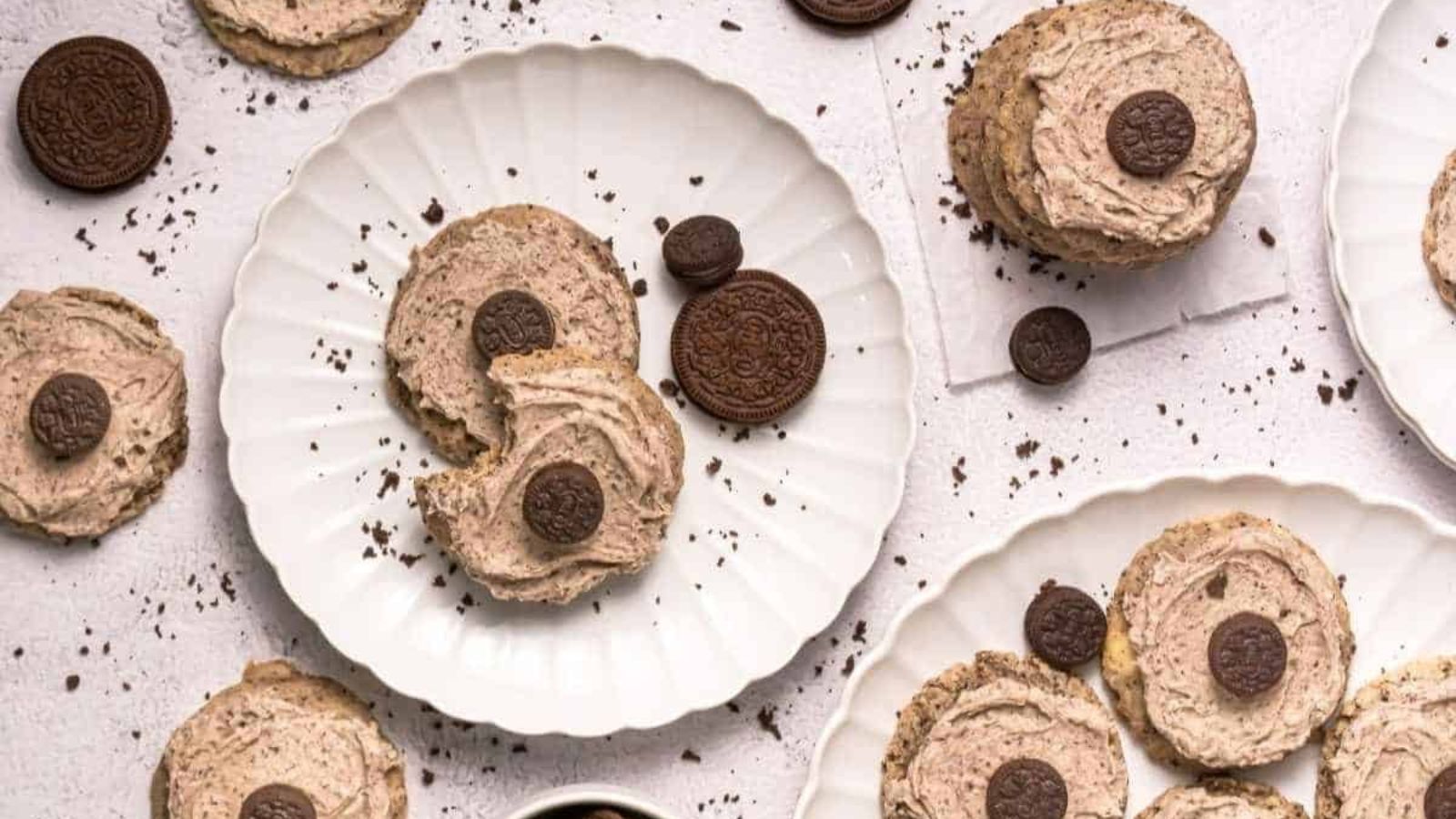 Copycat Crumbl Cookies and Cream Milkshake Cookies arranged on white plates and a light surface with cookie crumbs scattered around.