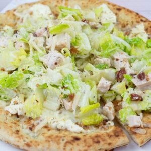 A pizza topped with chopped romaine lettuce, grilled chicken pieces, and a creamy dressing, served on a white plate.