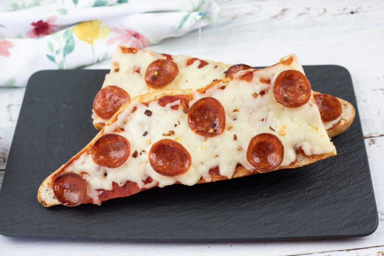 Two slices of French bread pizza topped with melted cheese and pepperoni are placed on a black rectangular plate.