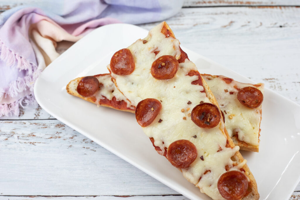 Two slices of French bread pizza topped with melted cheese and pepperoni on a white rectangular plate.