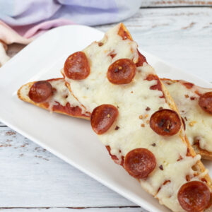 Two slices of French bread pizza topped with melted cheese and pepperoni on a white rectangular plate.