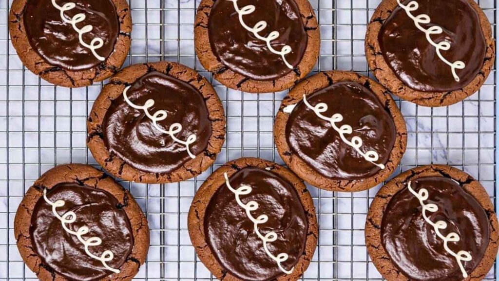 Nine chocolate cookies with glossy chocolate icing and white icing swirl on top, arranged on a wire cooling rack.