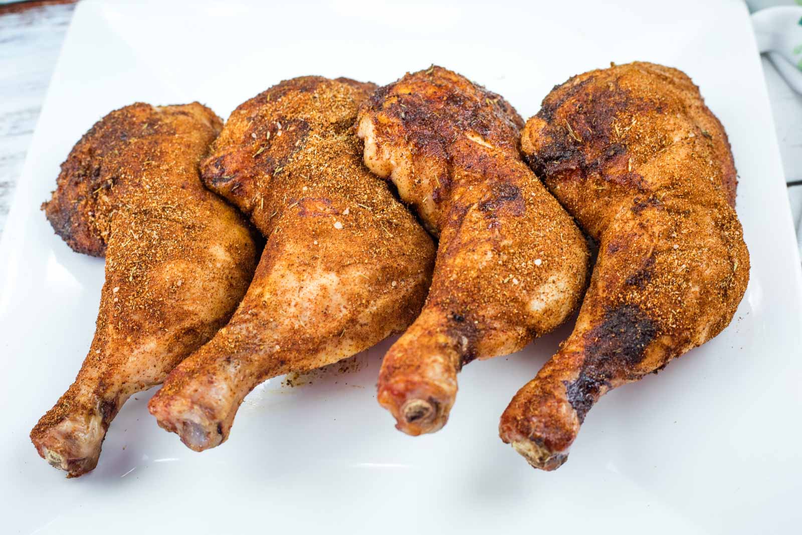 Four Smoked Chicken Leg Quarters are arranged in a row on a white plate.